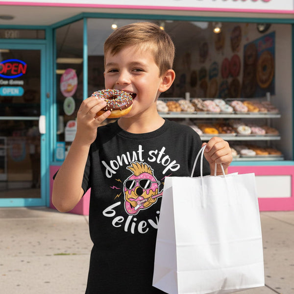 Child eating a donut and holding a bag in front of a donut shop.
